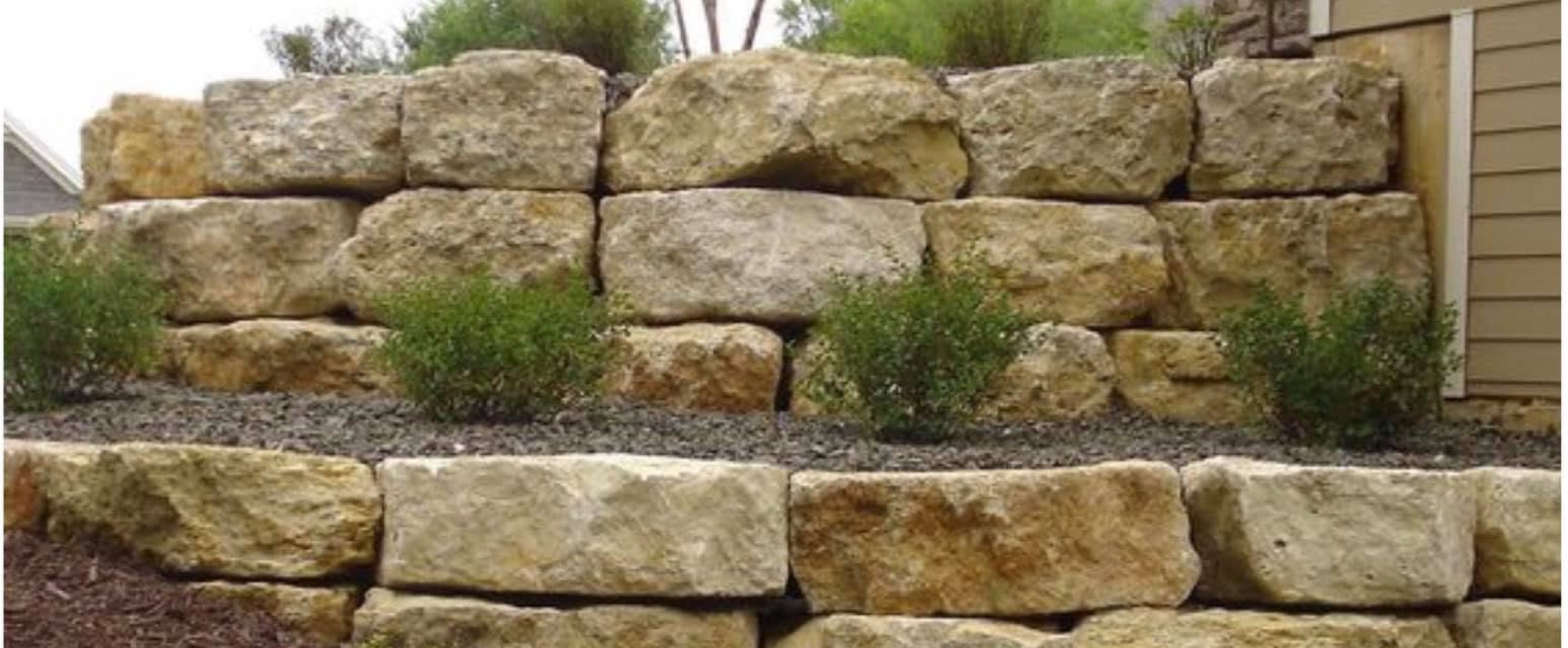 A sandstone retaining wall with garden plants, landscaping supplied by Macca's Mulch Firewood & Gravel