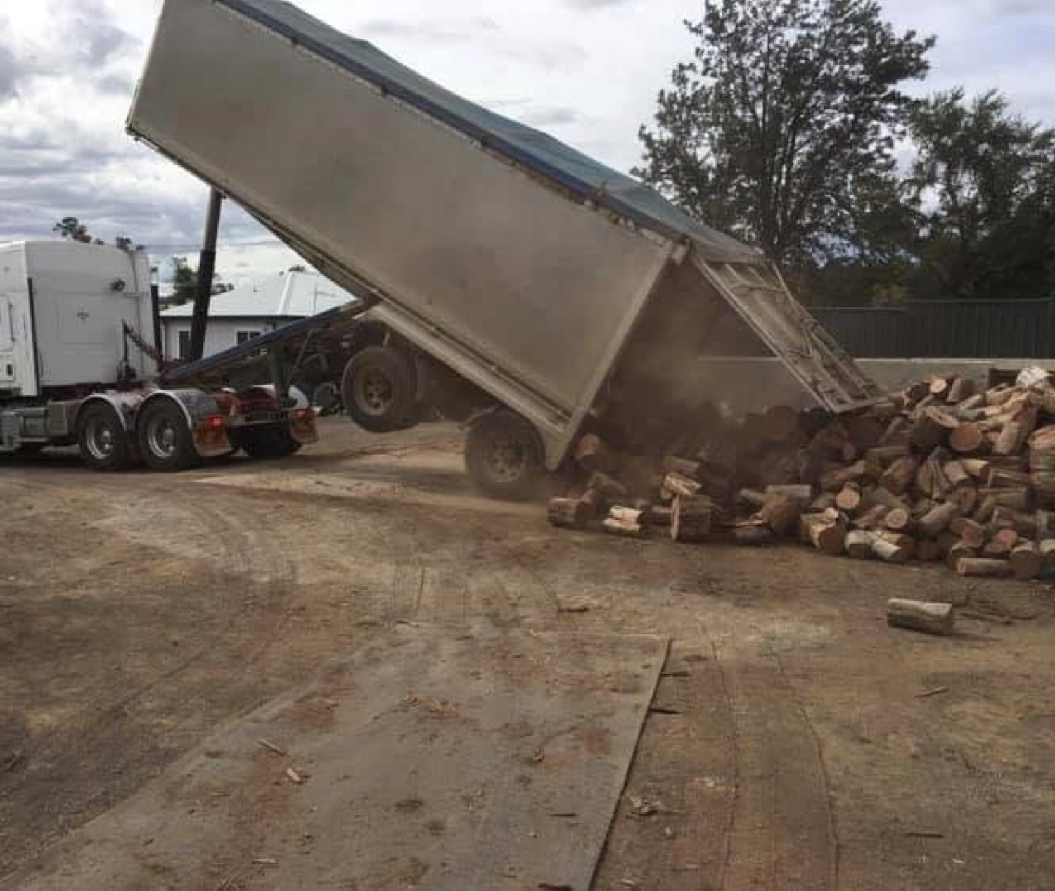 A semi-trailer tipping a bulk load of firewood rounds into the yard